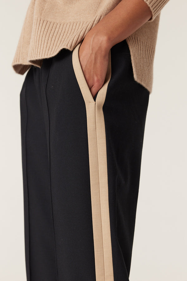 Navy Leah Pant with tan side stripe and a hand in the pocket, paired with a beige sweater.