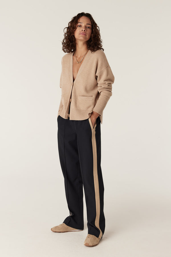 Woman in navy Leah pants with tan side stripe, beige cardigan, and tan shoes.