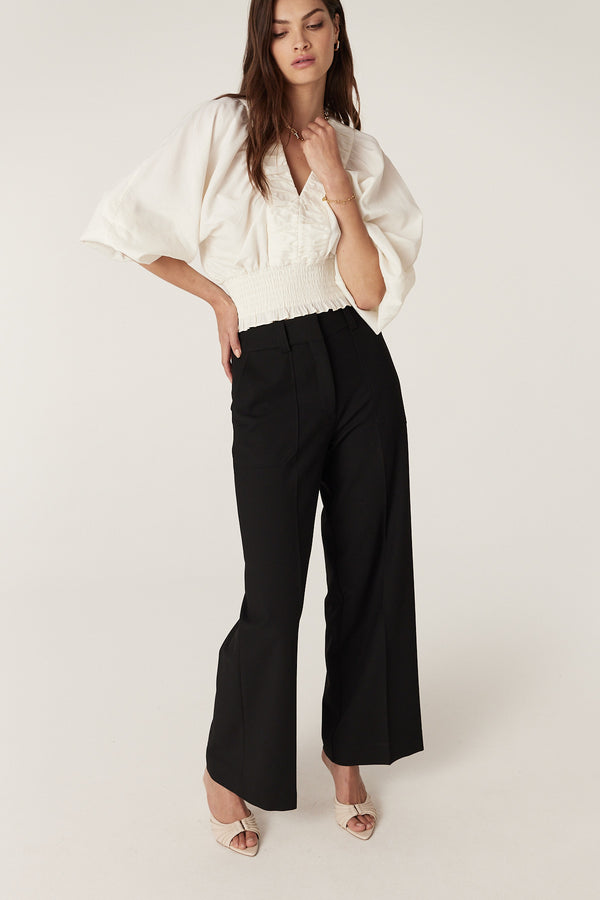 Model wears ecru Sasha Blouse with V-neck, ruched detail, wide batwing sleeves, and shirred waist.