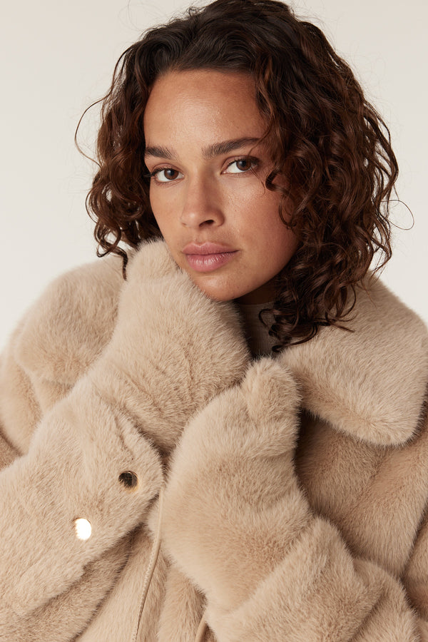 Camel faux fur mittens with gold snap closure, worn by a woman in a matching coat.