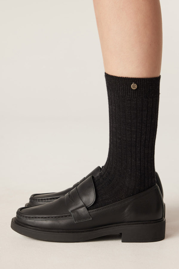Charcoal ribbed merino wool socks with a small gold logo, worn with black leather loafers.