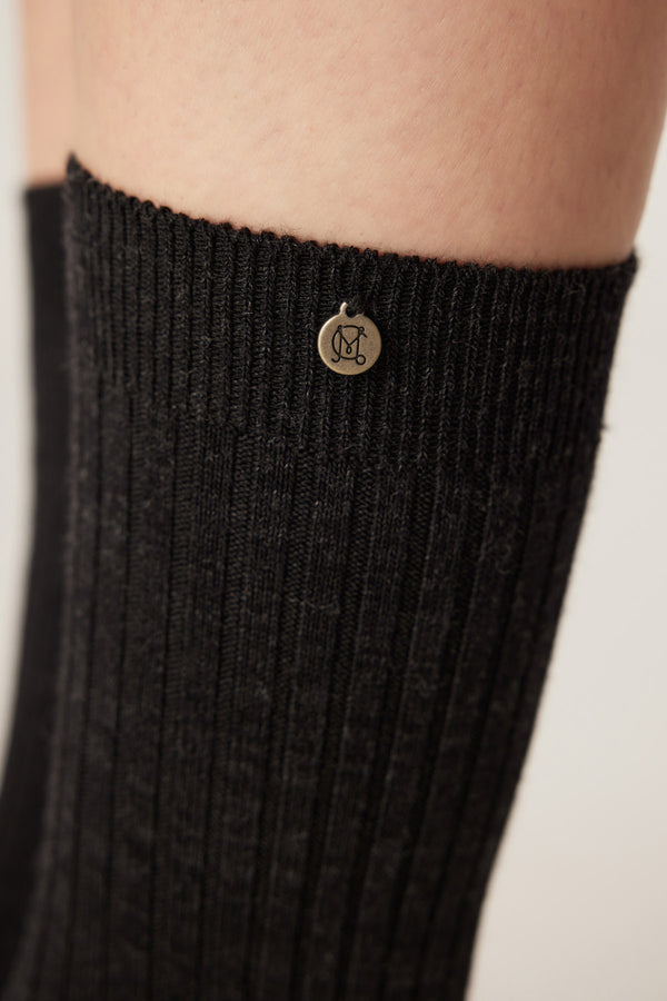 Charcoal Merino ribbed sock with a small silver logo charm near the cuff.