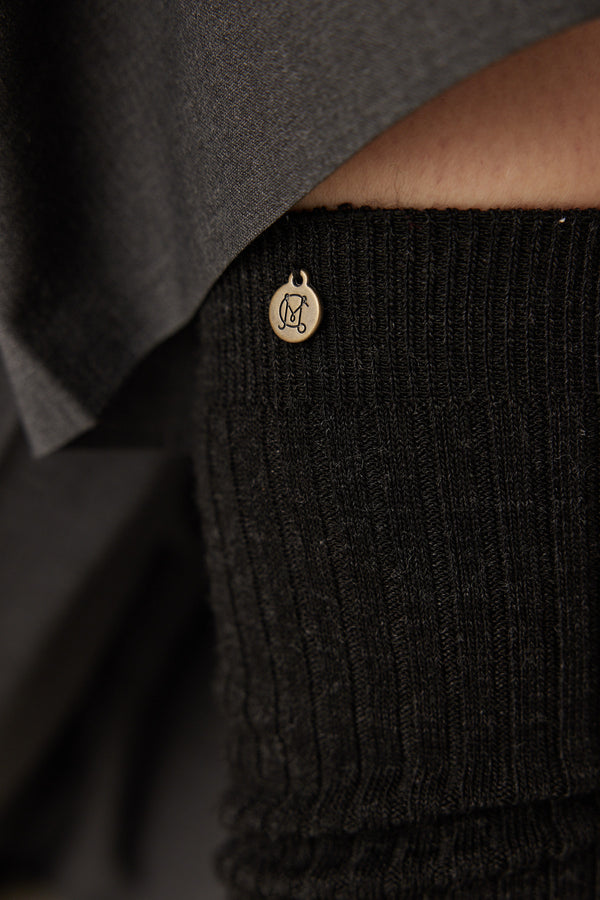 Charcoal ribbed merino wool sock with a small gold charm featuring an "M" logo.