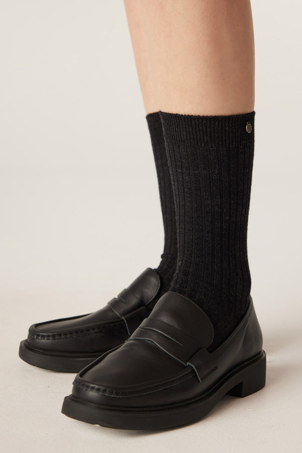 Charcoal ribbed merino wool socks paired with black leather loafers, featuring a subtle brand button.