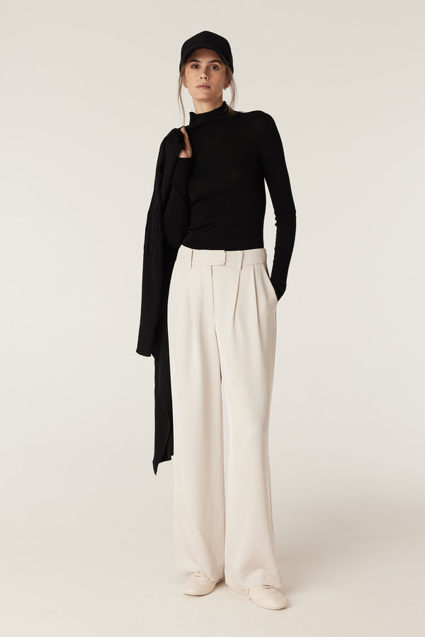 Woman in a black superfine merino wool turtleneck, cream wide-leg pants, and a black cap.