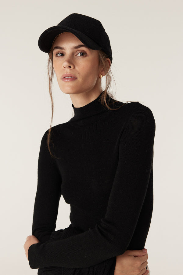 Woman in a black superfine merino wool slim-fit turtleneck and black cap.