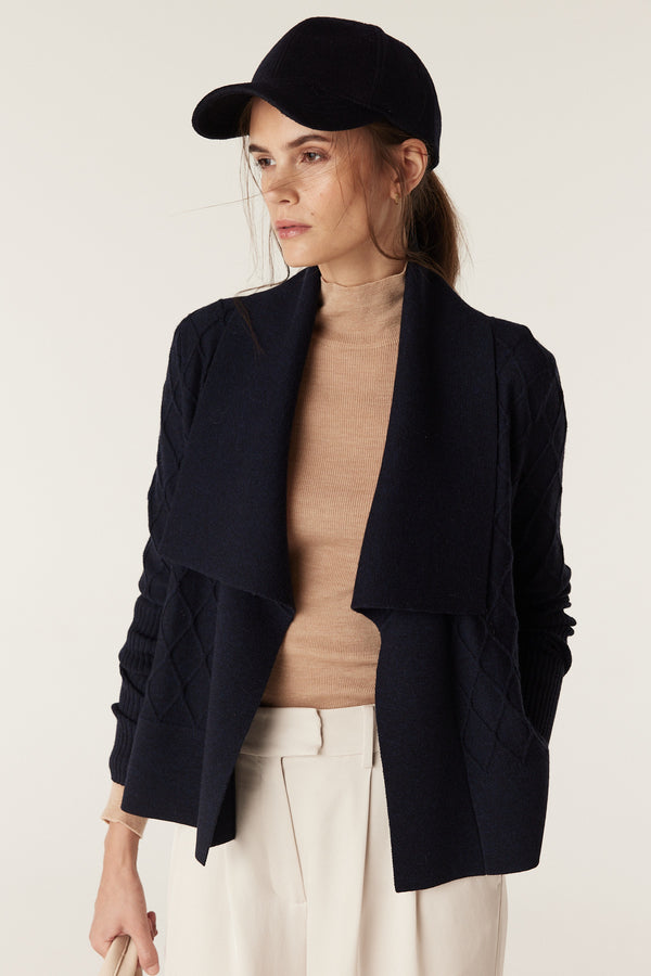Model wears a slim-fit latte merino wool turtleneck under a navy cardigan and cream pants.