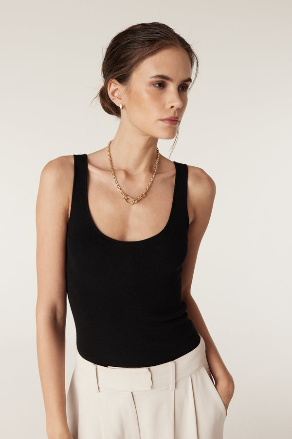 Woman wearing a black superfine merino wool singlet with a round neckline and a gold chain necklace.