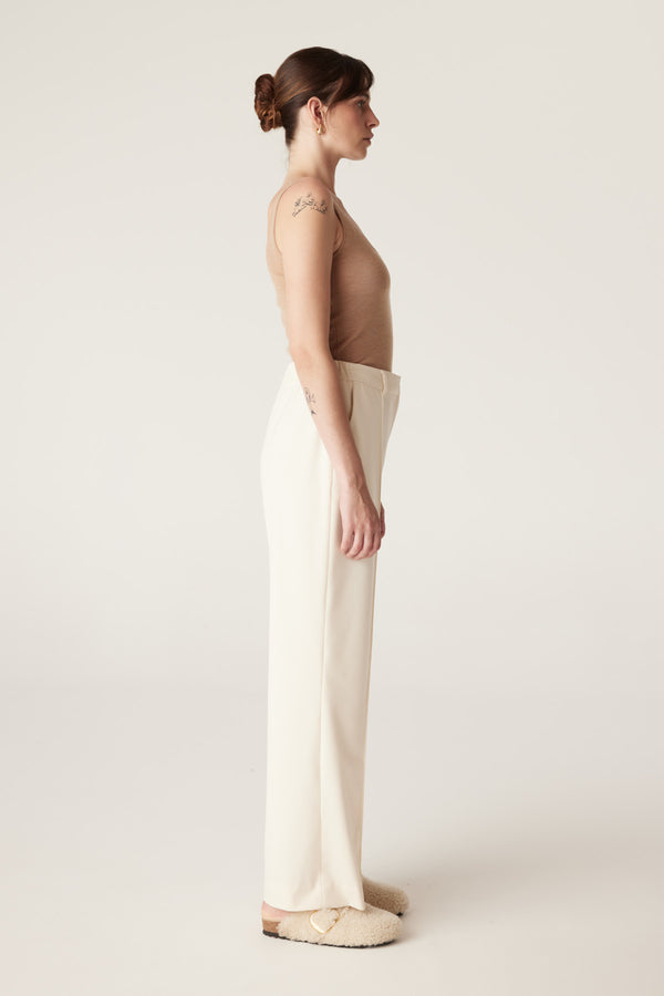 Woman in a camel superfine merino wool singlet with a round neckline, paired with cream pants.