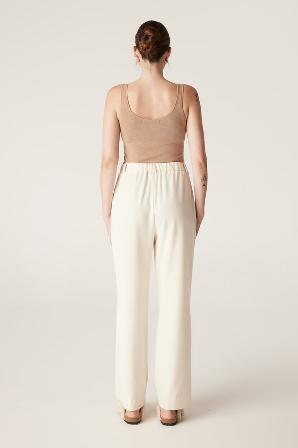 Woman from behind wearing a camel superfine merino wool singlet with a round neckline and cream wide-leg pants.