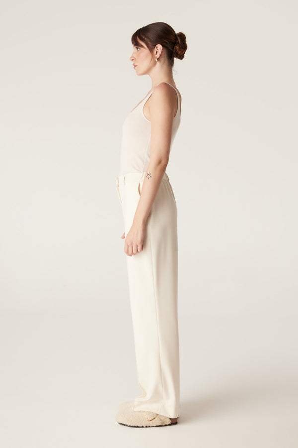 Model in an ecru superfine merino wool singlet with a round neckline, paired with cream trousers.