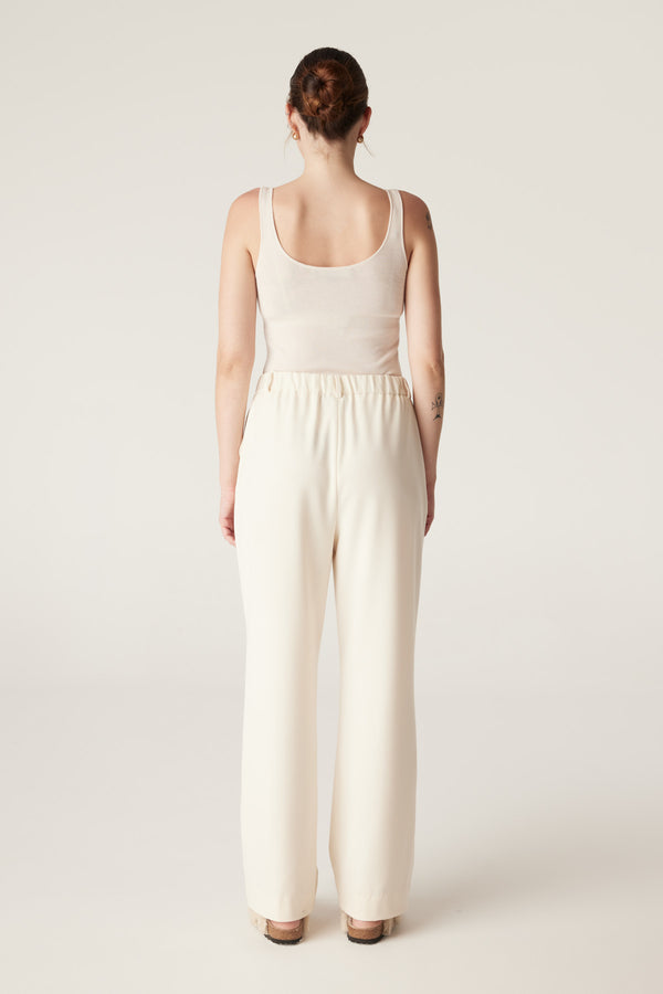 Woman from behind wearing an ecru superfine merino singlet with a round neckline and self-start hem.