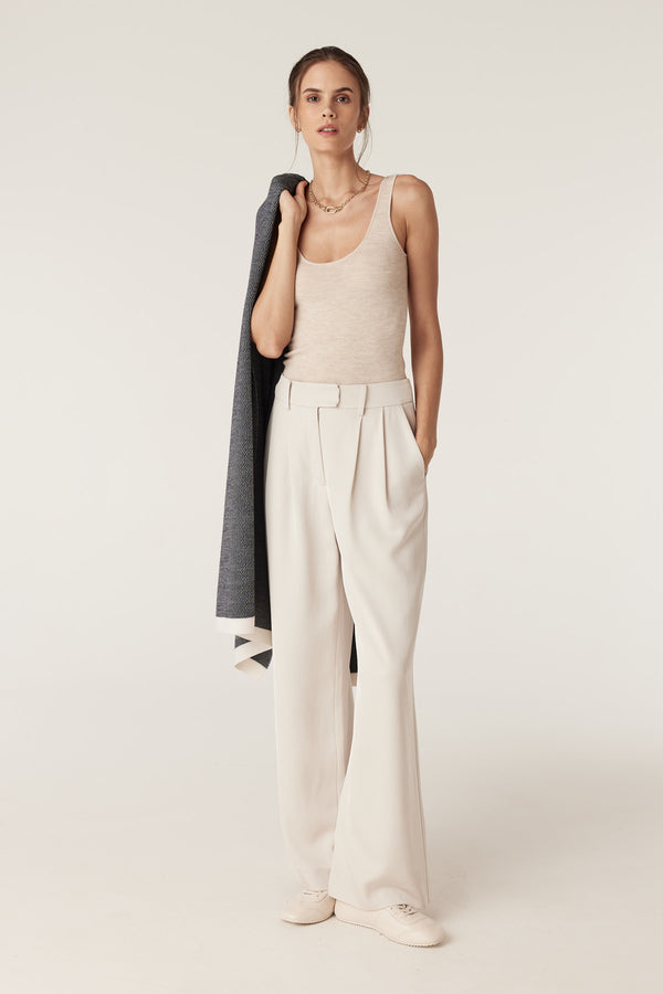 Woman wearing an oatmeal superfine merino singlet with a round neckline, light pants, and a jacket over her shoulder.