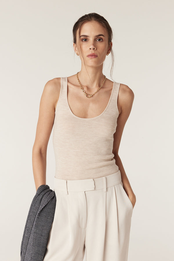 Woman wearing an oatmeal superfine merino wool singlet, light pants, and a gold necklace.