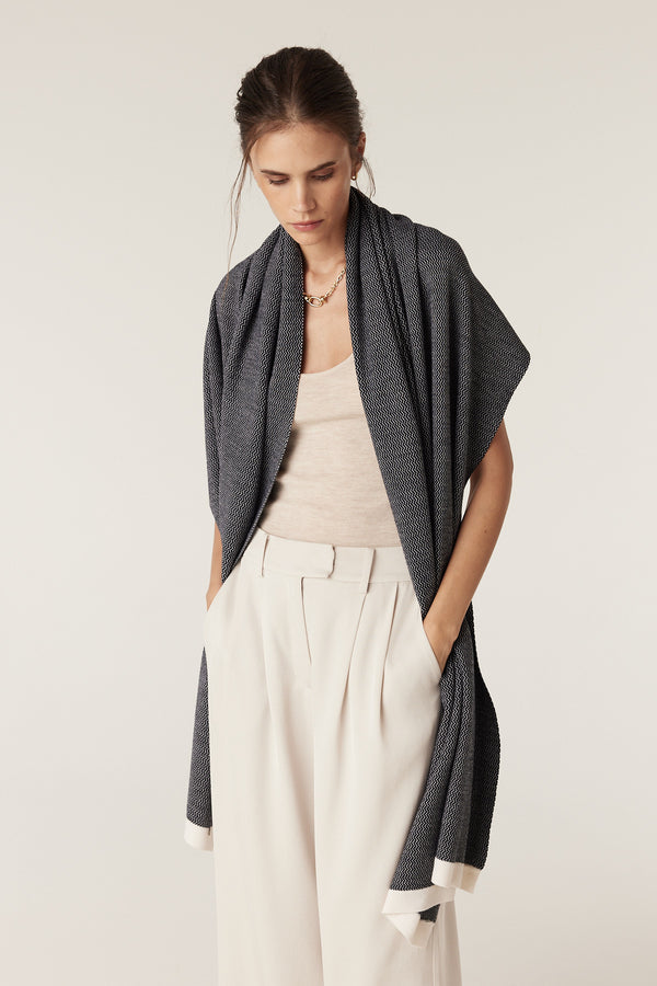 Woman in a slim-fit oatmeal merino singlet, white wide-leg pants, and a dark patterned scarf.