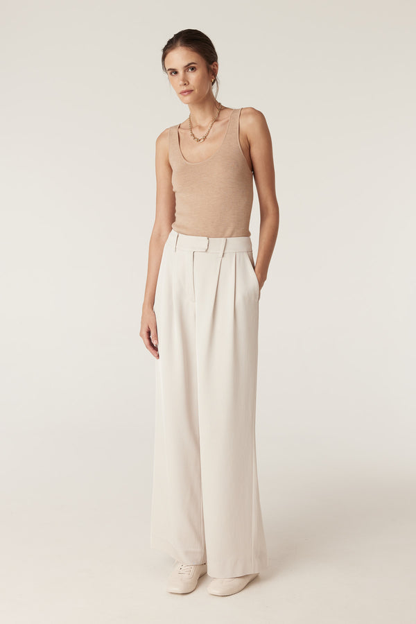 Woman wearing a slim-fit latte merino wool singlet with a round neckline and cream wide-leg pants.