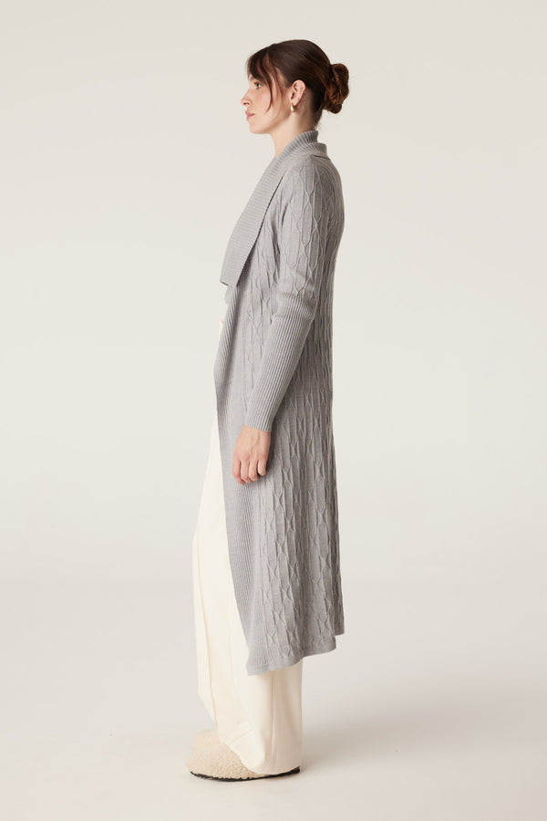 Woman wearing a longline grey marle merino wool cable knit cardigan with ribbed sleeves and collar.