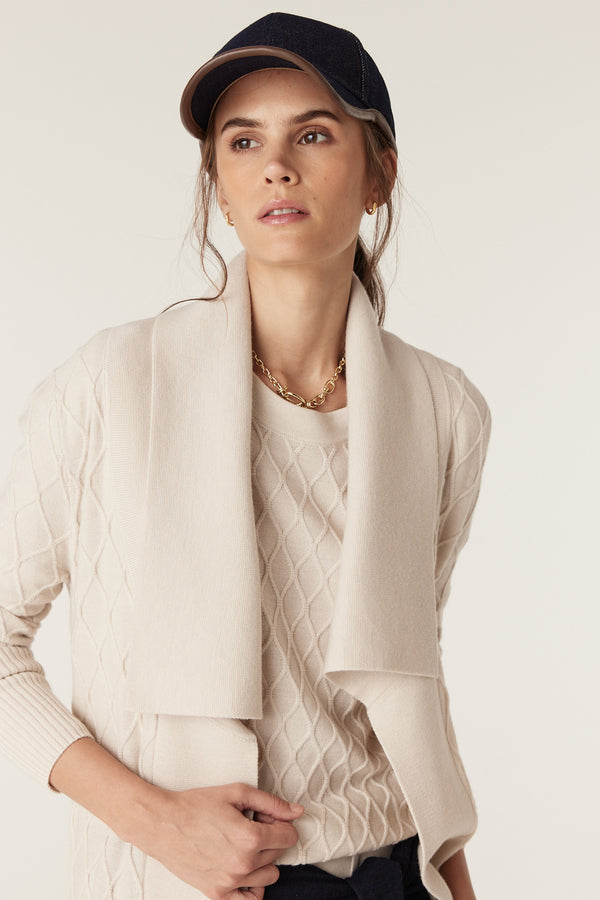 Woman in antique white merino wool cardigan with diamond cable stitch, Milano collar, and deep ribbed sleeves.