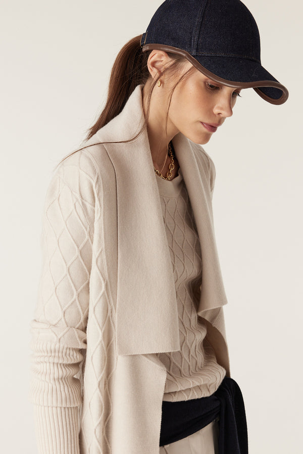 Woman in antique white Merino wool cardigan with diamond cable stitch, Milano collar, and deep ribbed sleeves.