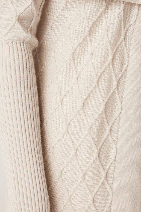 Close-up of an antique white Merino wool cardigan with diamond cable stitching and ribbed sleeve.