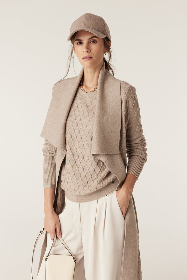 Woman in pebble Merino wool cardigan with diamond cable stitch, Milano collar, and detachable belt.