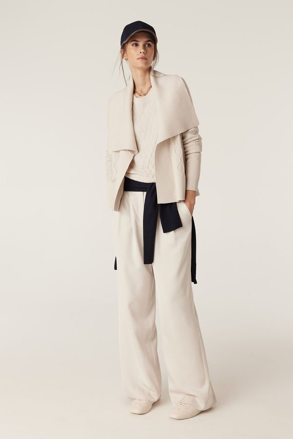 Woman in antique white merino wool cardigan with diamond cable stitch, Milano collar, and navy belt.