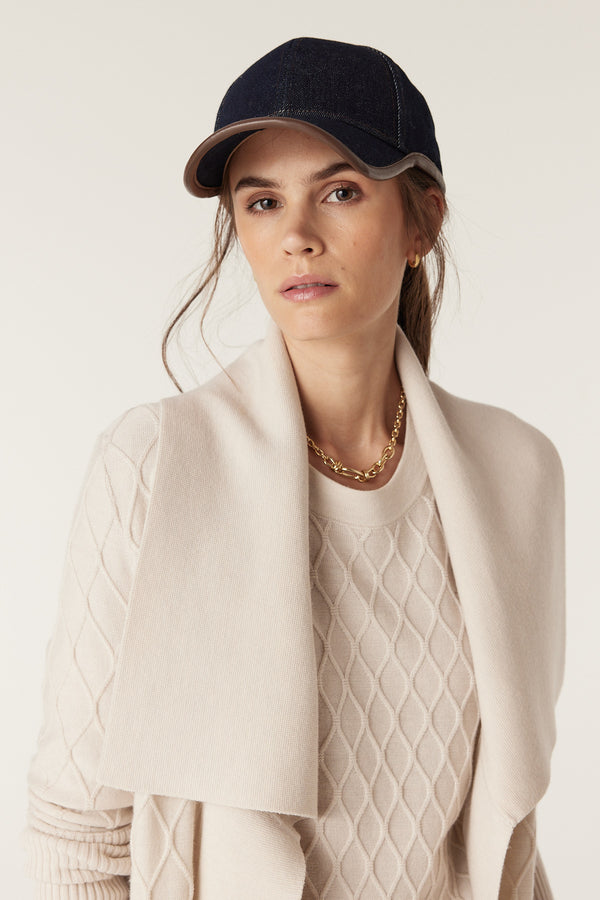 Woman in antique white merino wool cardigan with diamond cable stitch, Milano collar, and deep rib sleeves.
