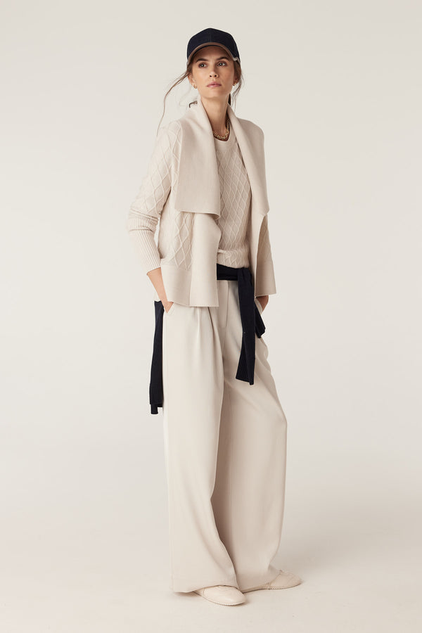 Woman in antique white merino wool cardigan with diamond cable stitch, Milano collar, and wide-leg pants.