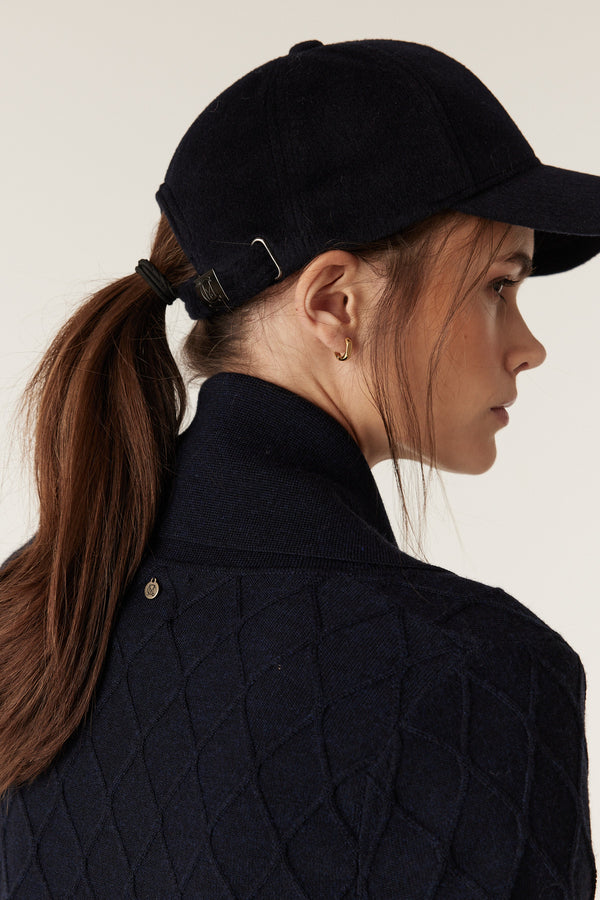 Woman in Midnight Navy Merino Wool cardigan with diamond cable stitch, Milano collar, and Heritage branded plate.