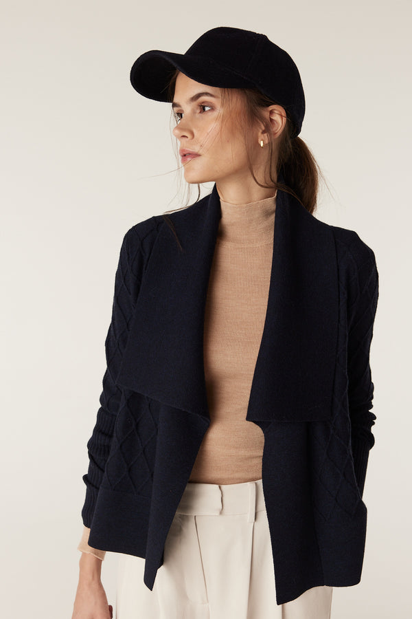Woman in Midnight Navy Merino wool cardigan with diamond cable stitching, Milano collar, and beige turtleneck.