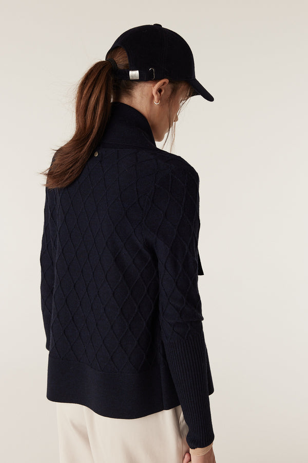 Woman in midnight navy Merino wool cardigan with diamond cable stitching, Milano collar, and deep ribbed sleeves.