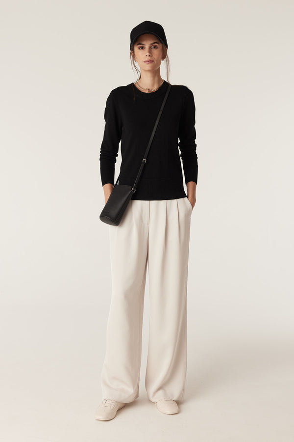 Woman wearing a black Merino wool crew neck jumper, light wide-leg trousers, and a black crossbody bag.