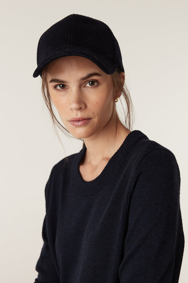 Woman wearing a Midnight Navy Merino wool crew neck jumper with a matching baseball cap.