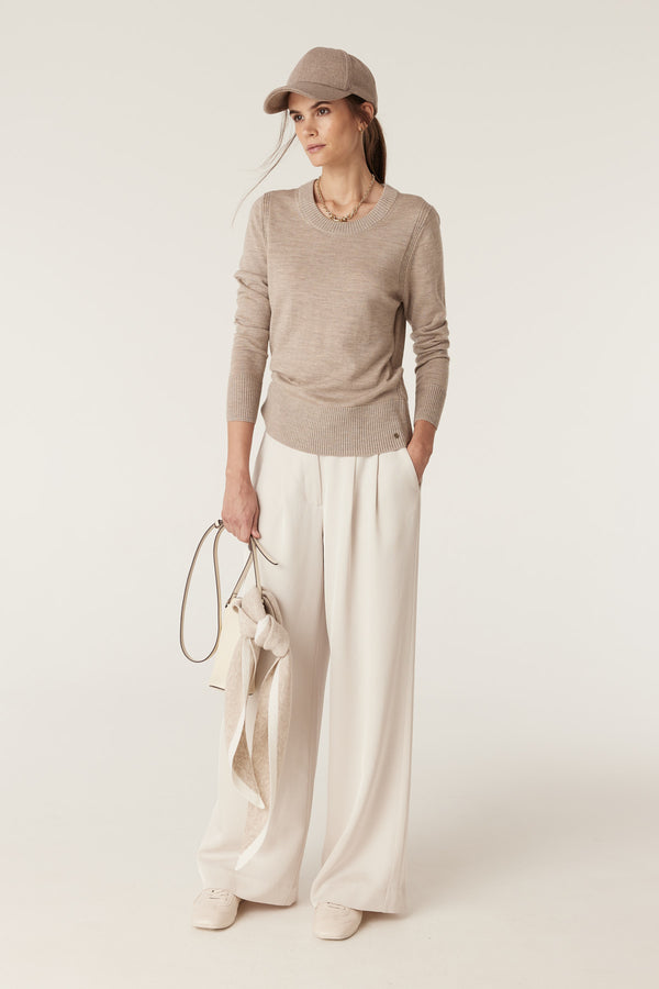 Woman wearing a pebble Merino wool crew neck jumper, cream wide-leg pants, and a matching cap.