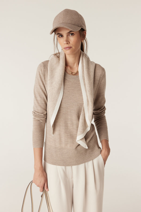 Woman in pebble merino wool crew neck jumper, white trousers, baseball cap, and scarf.