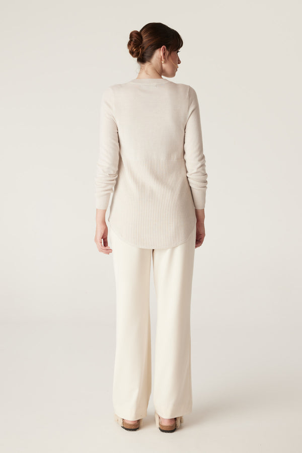 Woman in Antique White Merino Jumper with A-line shape, curved hem, and rib details on lower panel and sleeves.