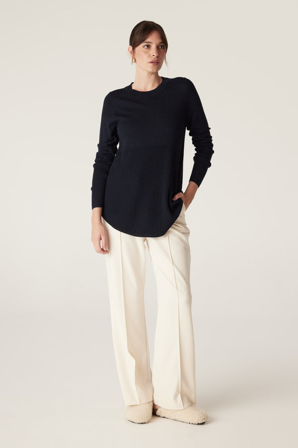 Woman wearing a Midnight Navy Merino wool jumper with A-line shape, curved hem, and rib detailing.