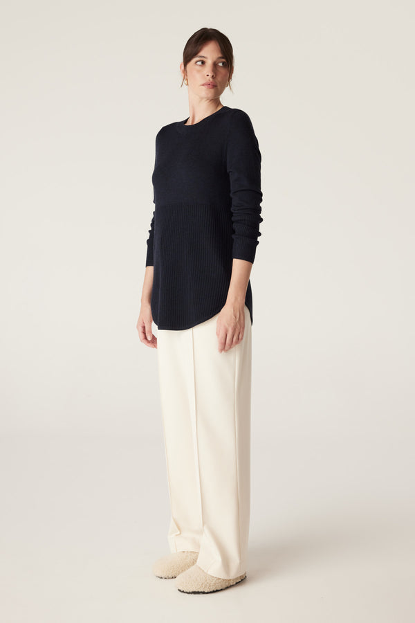 Woman wearing a Midnight Navy Merino wool jumper with ribbed lower panel, curved hem, and cream trousers.