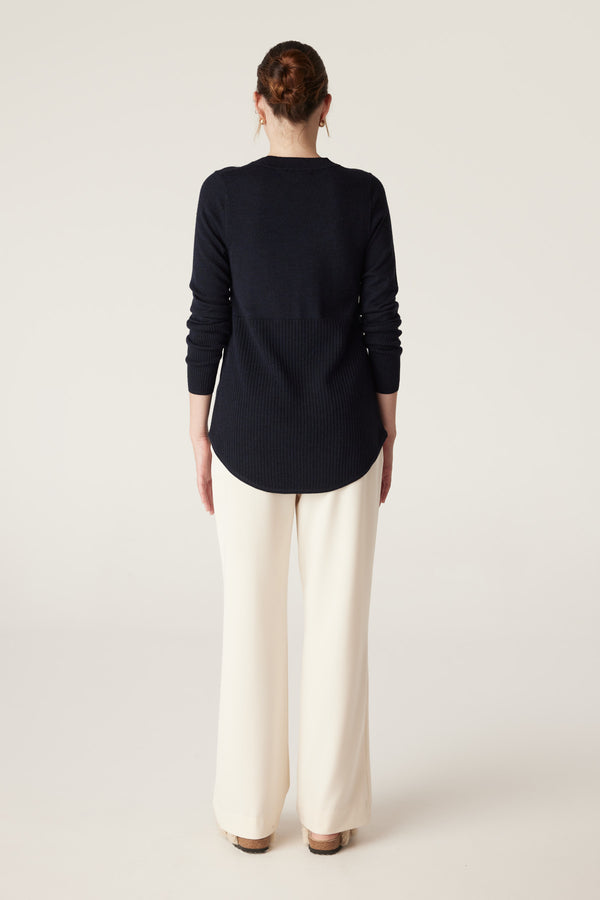 Model from behind wearing a Midnight Navy Merino wool jumper with an A-line shape, curved hem, and ribbed lower panel.