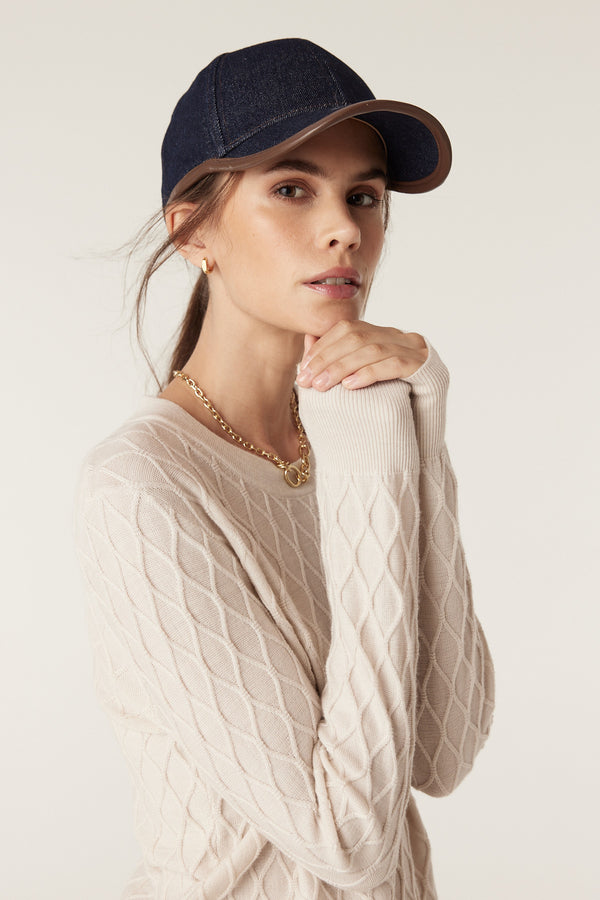 Woman in antique white merino wool jumper with diamond cable stitch, wearing a navy cap.