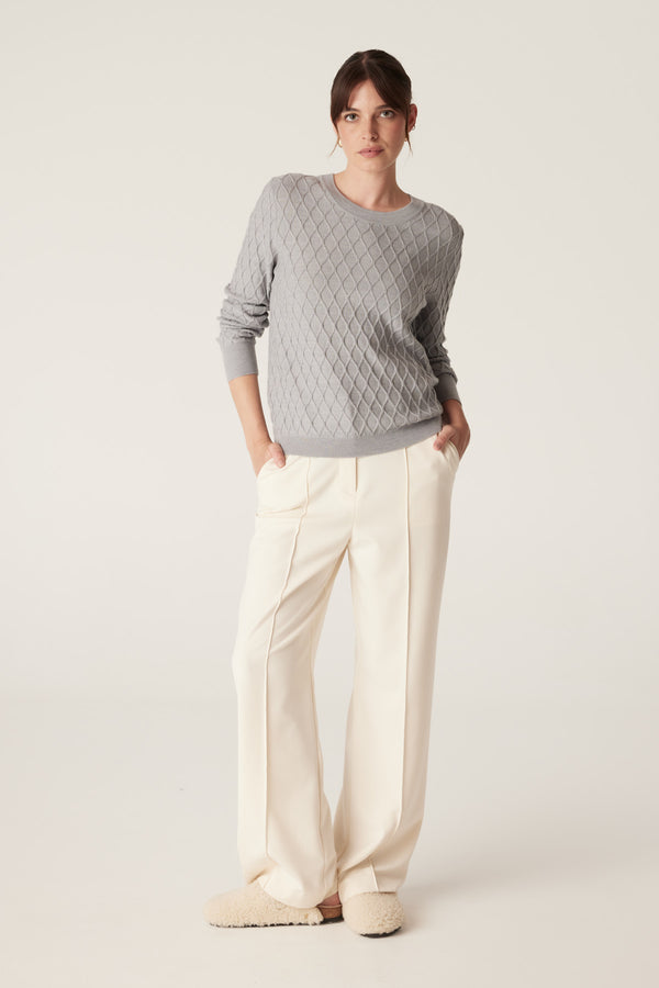 Model wears a grey marle Merino wool jumper with diamond cable knit and cream wide-leg pants.