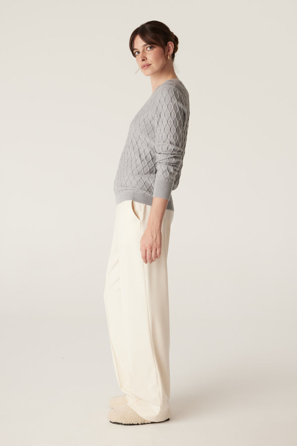 Model in a grey marle merino wool jumper with diamond cable stitch and cream wide-leg pants.