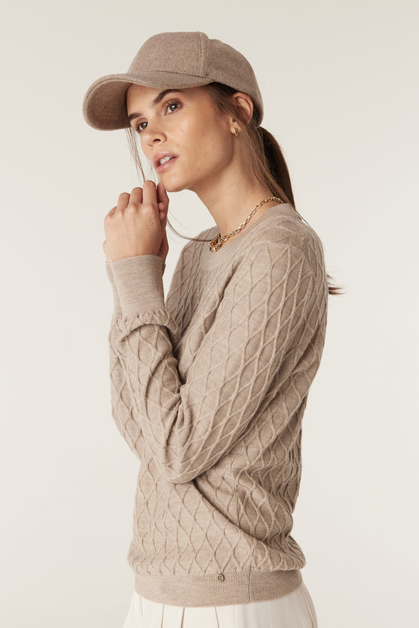 Woman wearing a pebble merino wool jumper with diamond cable stitch, crew neck, and rib trims.