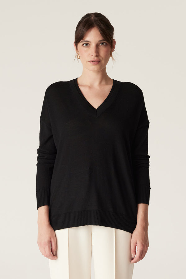 Woman wearing a black fine merino wool V-neck jumper with dropped shoulders and rib trim.