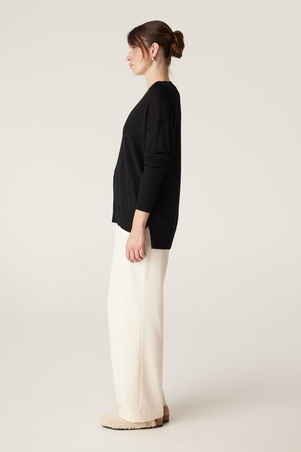 Woman in a black V-neck merino wool jumper with dropped shoulders and a high-low hem.
