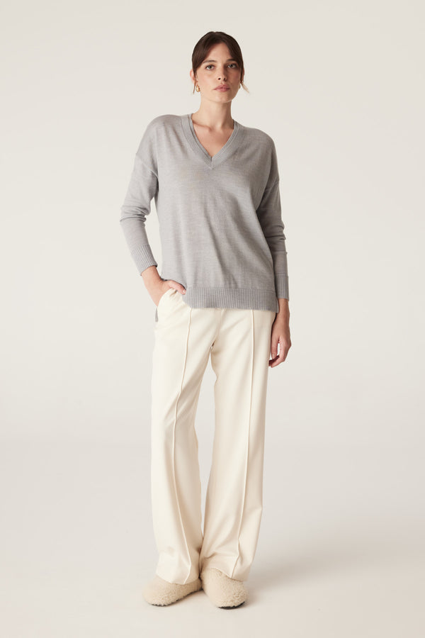 Woman in a grey marle merino wool V-neck jumper with dropped shoulders and cream wide-leg pants.