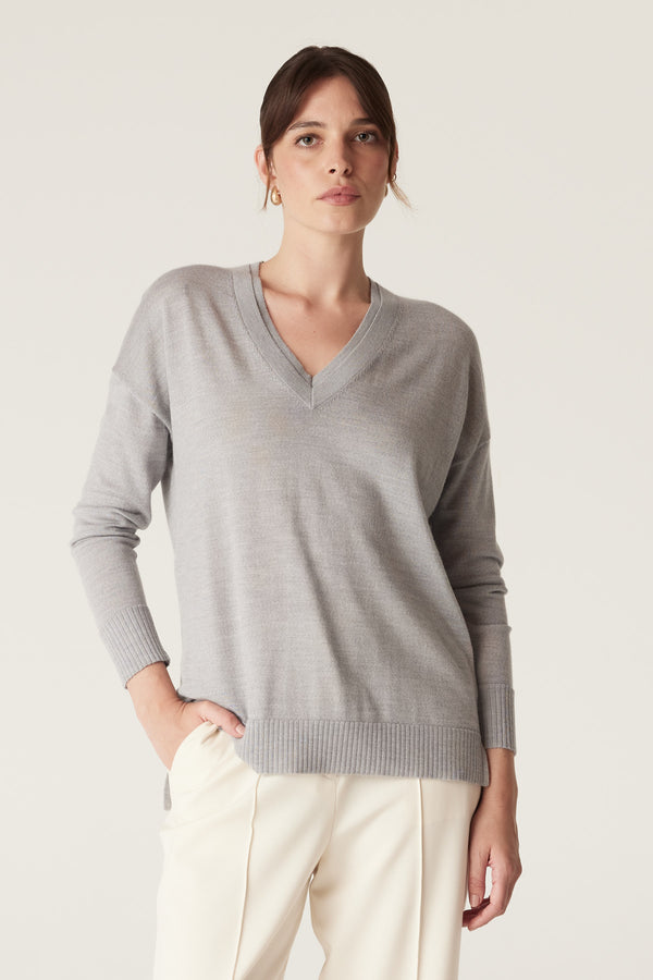 Model wears a grey marle merino wool V-neck jumper with dropped shoulders and ribbed cuffs, paired with cream pants.