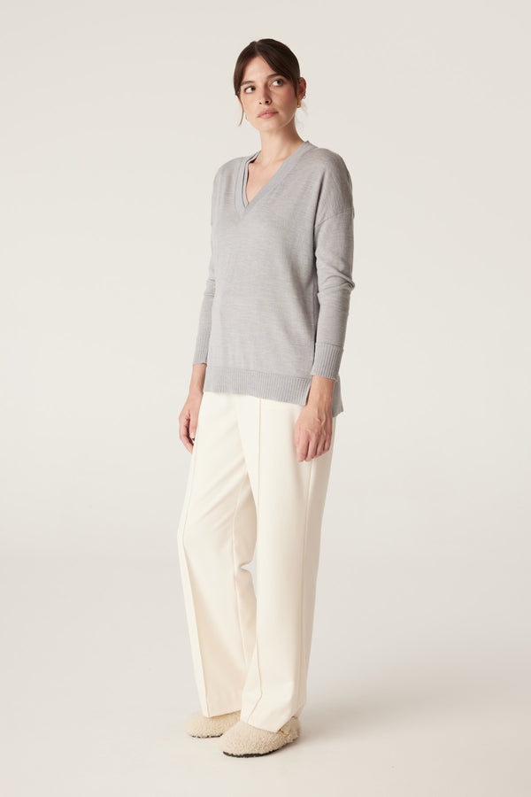 Woman in a grey marle merino wool V-neck jumper with a high-low hem, side splits, and dropped shoulders.