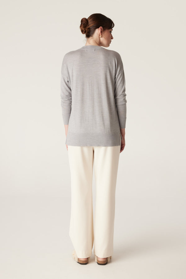 Model from behind wearing a grey marle merino wool V-neck jumper with a high-low hem and cream pants.