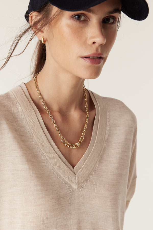 Woman wearing an oatmeal fine merino wool V-neck jumper with double collar trim and a gold chain necklace.
